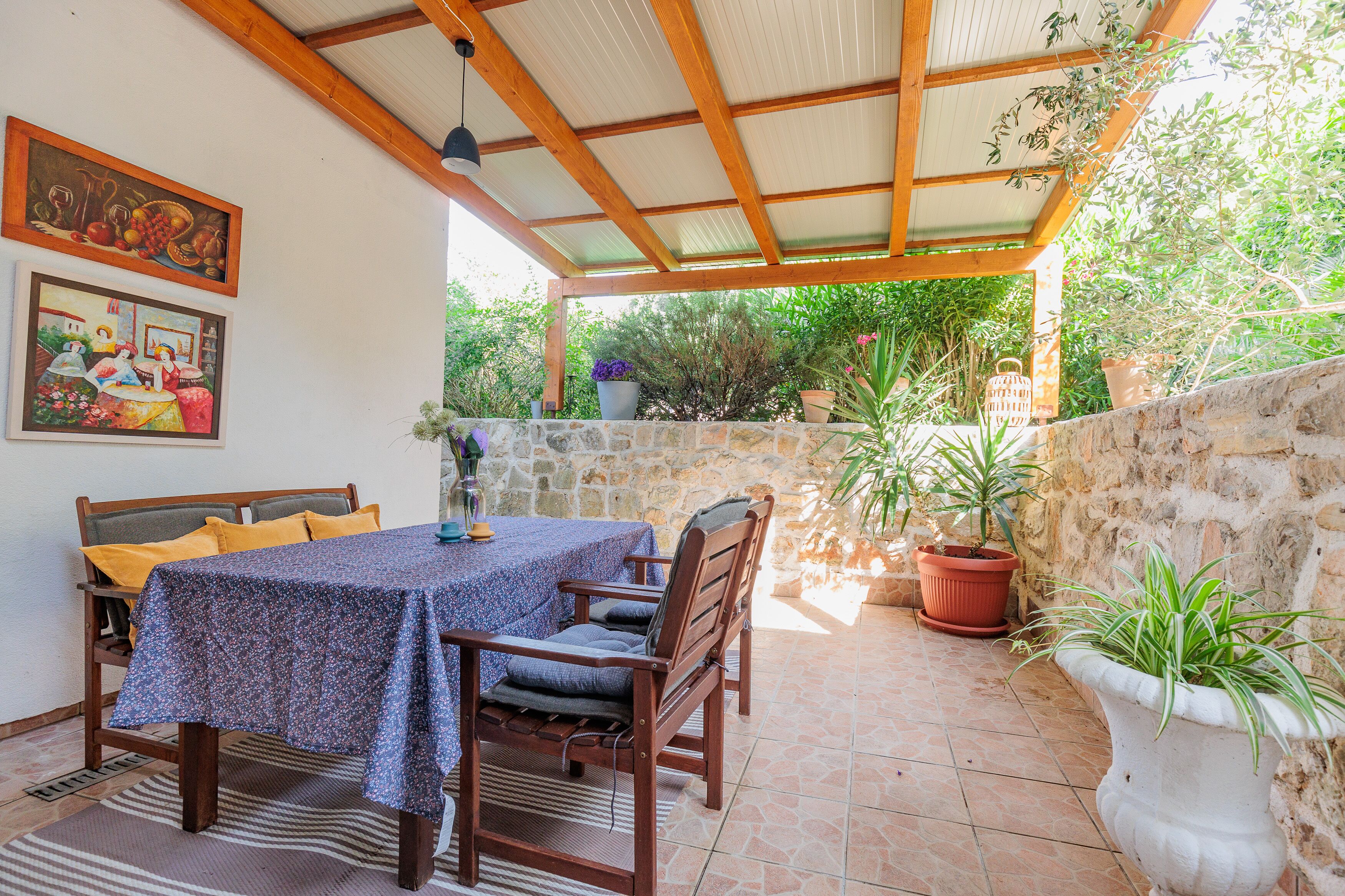 A covered patio with a table and chairs, stone walls, and potted plants.