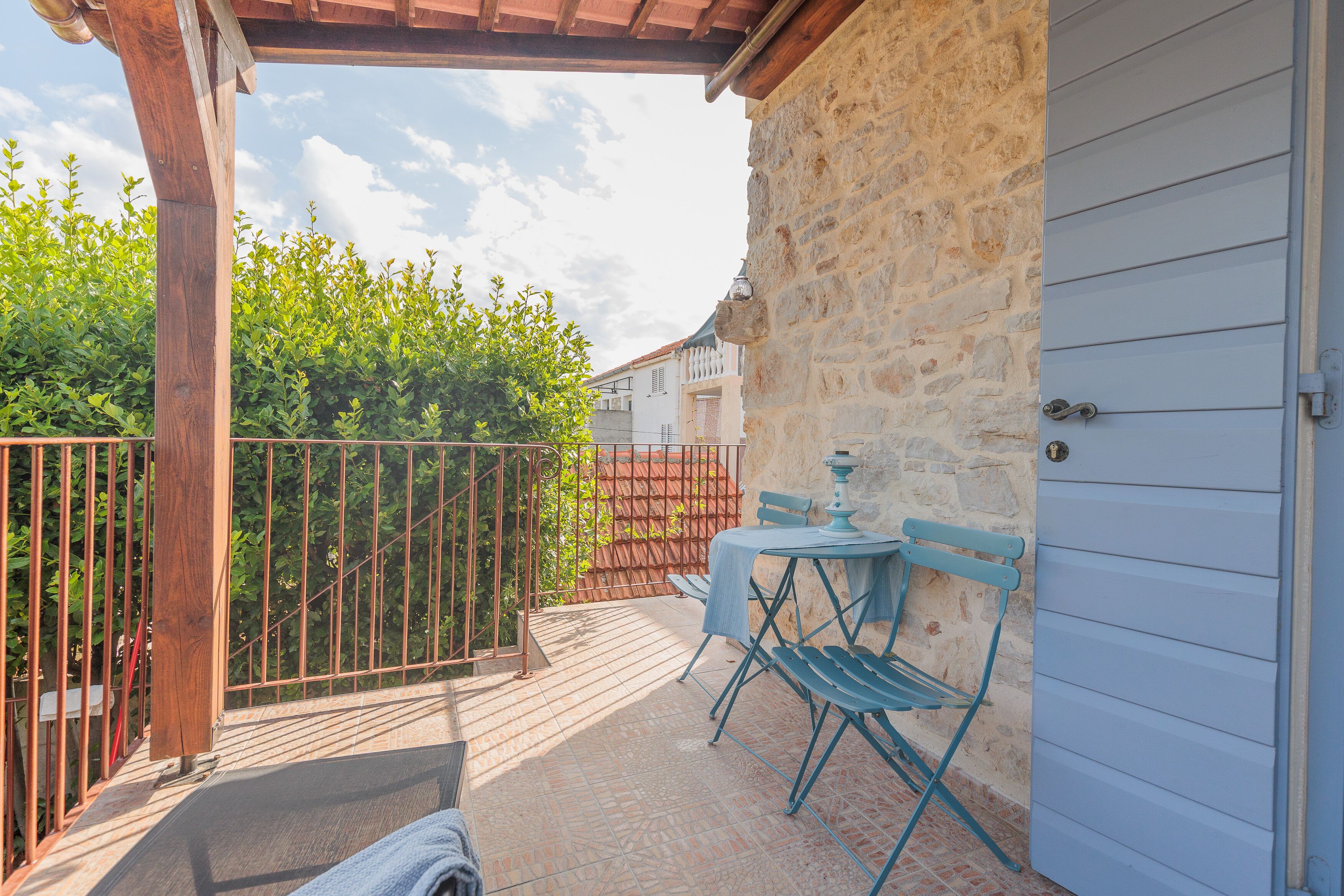 Une terrasse extérieure couverte, dotée d’un mur en pierre, d’une rambarde en métal et d’une table avec des chaises.