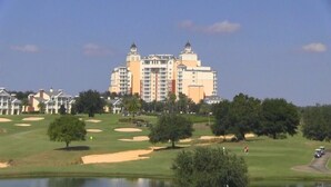 Un grand hôtel à étages, doté d’une tour centrale, entouré d’un parcours de golf avec des bunkers de sable et des arbres.