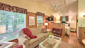 Ein gemütliches Wohnzimmer mit einer Couch, einem Couchtisch und einem Fernseher. Es gibt ein Bett mit Kopfteil und einen kleinen Tisch mit Lampe.
