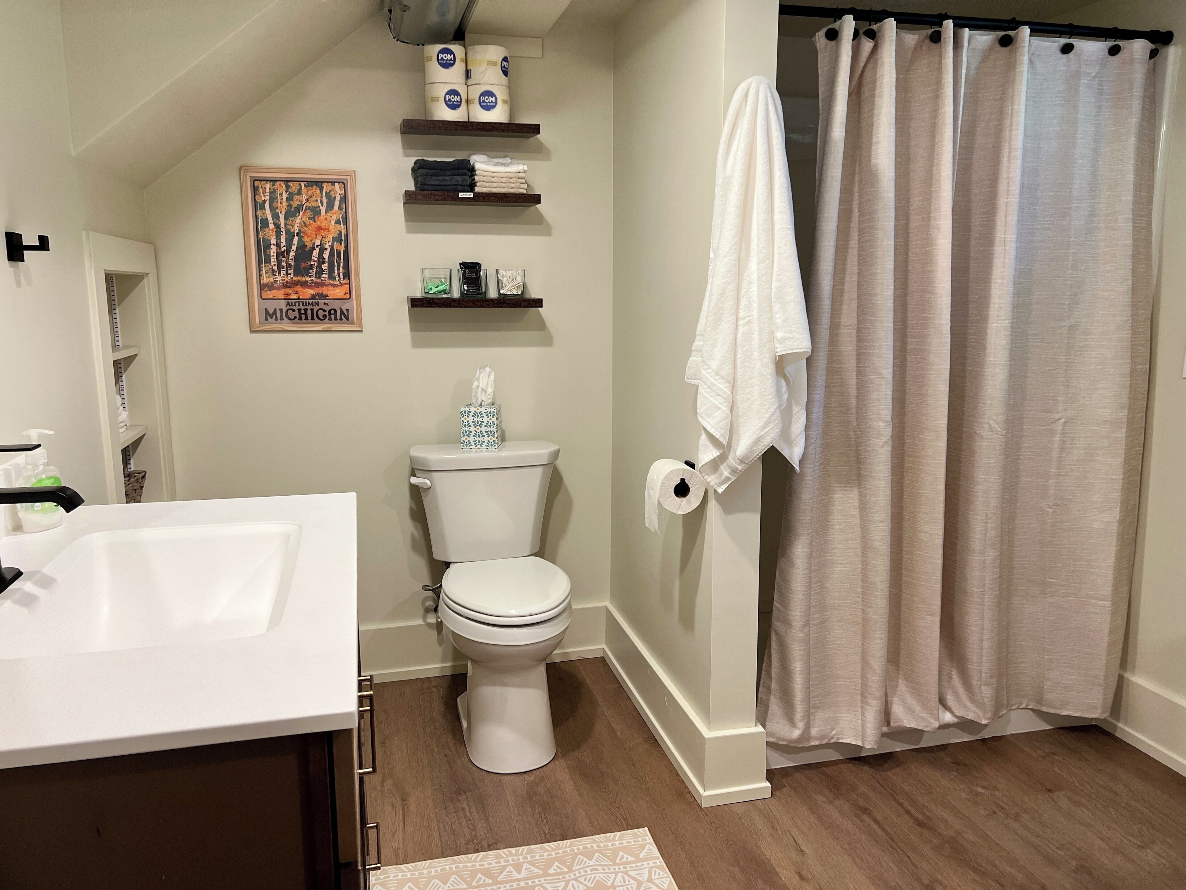 A bathroom with a toilet, a sink, a shower curtain, and shelves with toiletries.