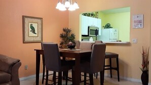 Ein Essbereich mit Tisch und Stühlen, einer Couch, einem gerahmten Bild an der Wand und einer Küche im Hintergrund.