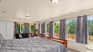 Quarto com cama grande, mesa de cabeceira, cadeira e varanda com cortinas.
