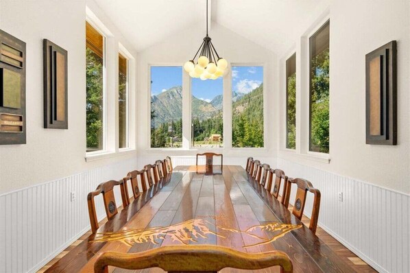 A long dining table with chairs, large windows, and a mountain view.