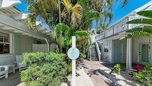A white building with a covered deck and a sign indicating amenities like a cabin, beach, and crow's nest. - Spinnakers Cottages - Cabin 1 - Dog Friendly - 250 Steps to Beach, Pool (Holmes Beach)