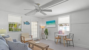 A living room with a sofa, chairs, a coffee table, a ceiling fan, and a TV. - Spinnakers Cottages - Cabin 1 - Dog Friendly - 250 Steps to Beach, Pool (Holmes Beach)