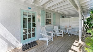 A covered outdoor seating area with white furniture and a wooden deck. - Spinnakers Cottages - Cabin 1 - Dog Friendly - 250 Steps to Beach, Pool (Holmes Beach)