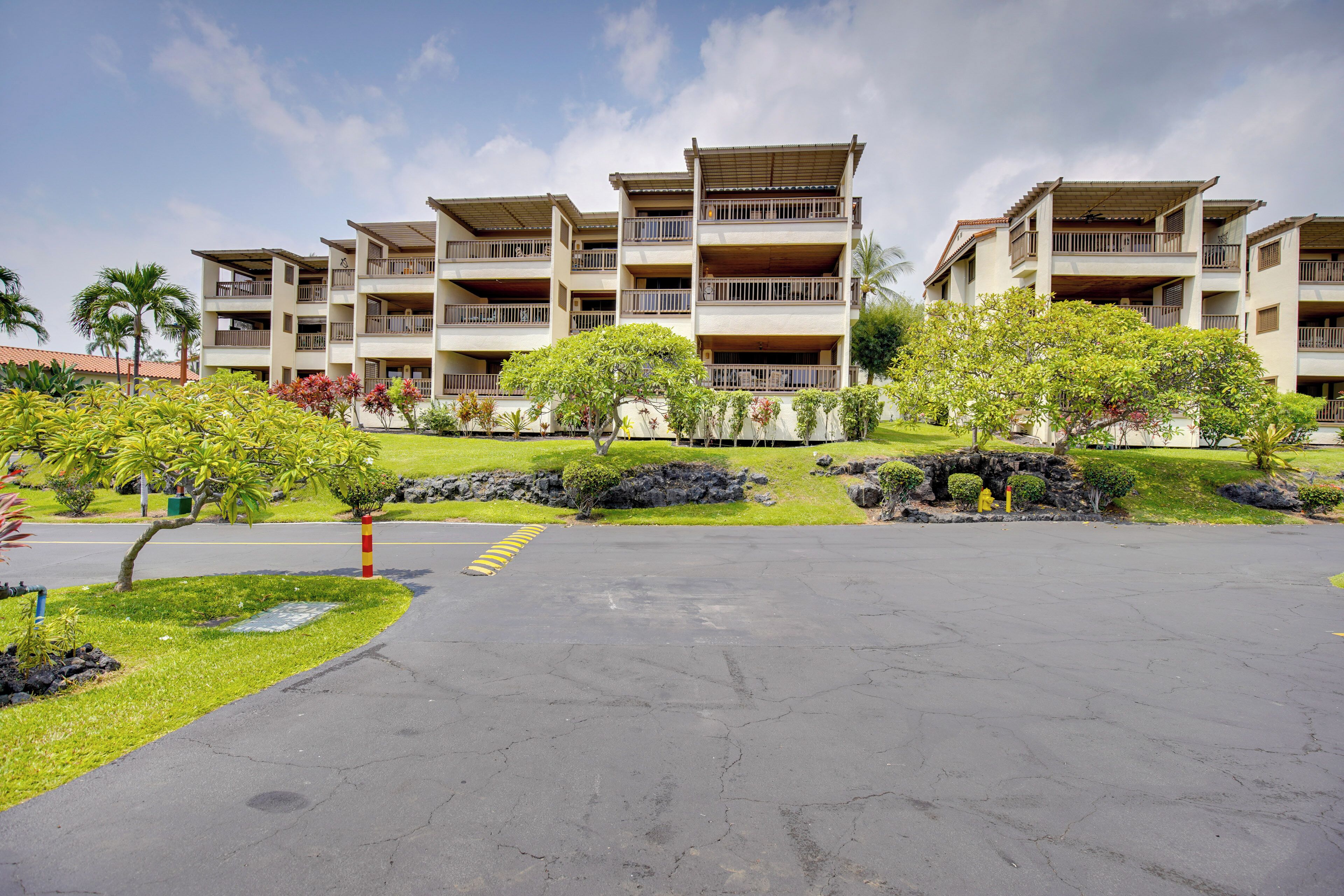 Een hotel met meerdere verdiepingen, balkons en een parkeerplaats met een aangelegde tuin.