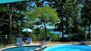A swimming pool with lounge chairs and umbrellas, surrounded by trees and a fence.