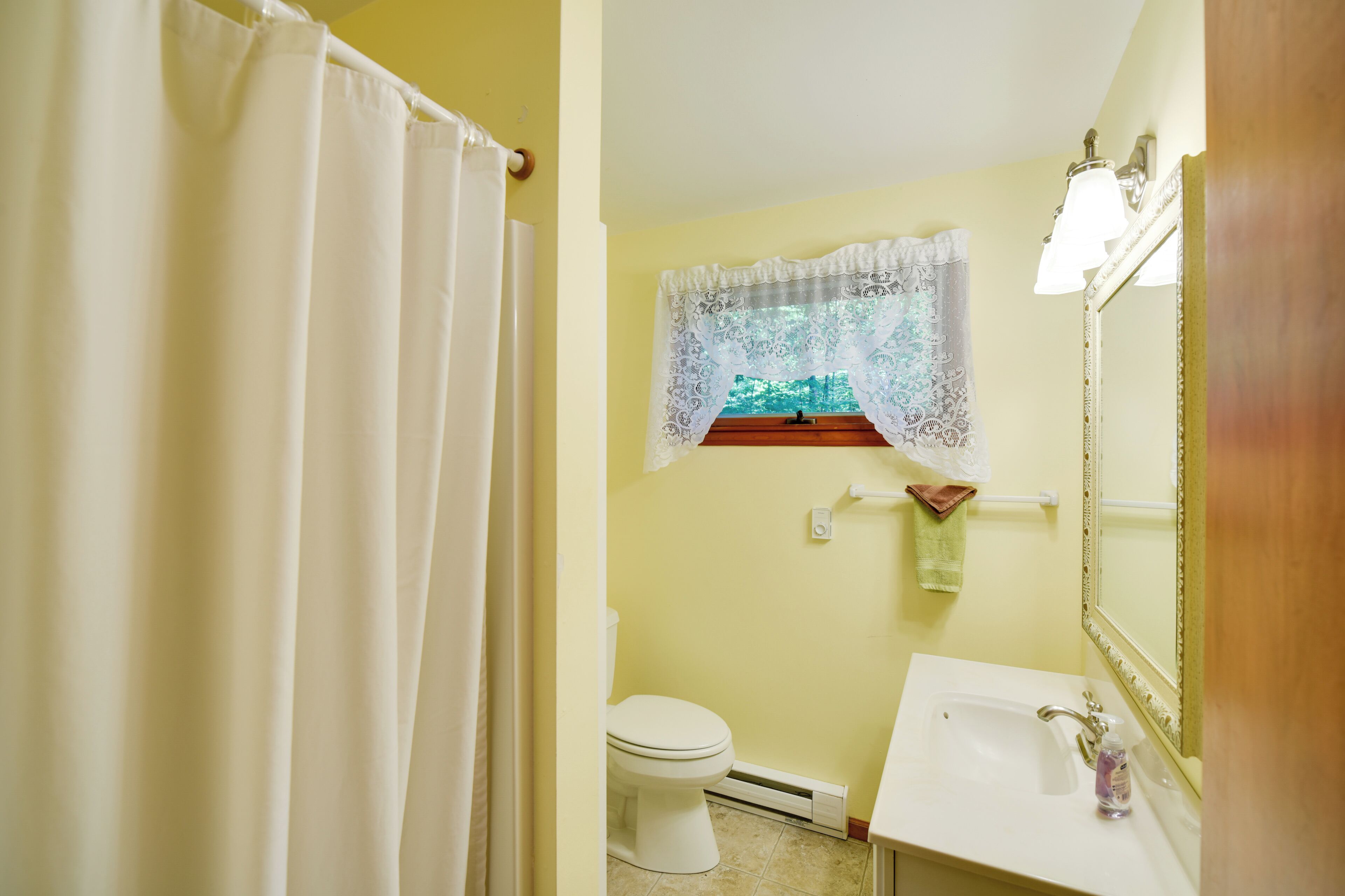Une salle de bain avec des toilettes, un lavabo et une fenêtre ornée de rideaux en dentelle.