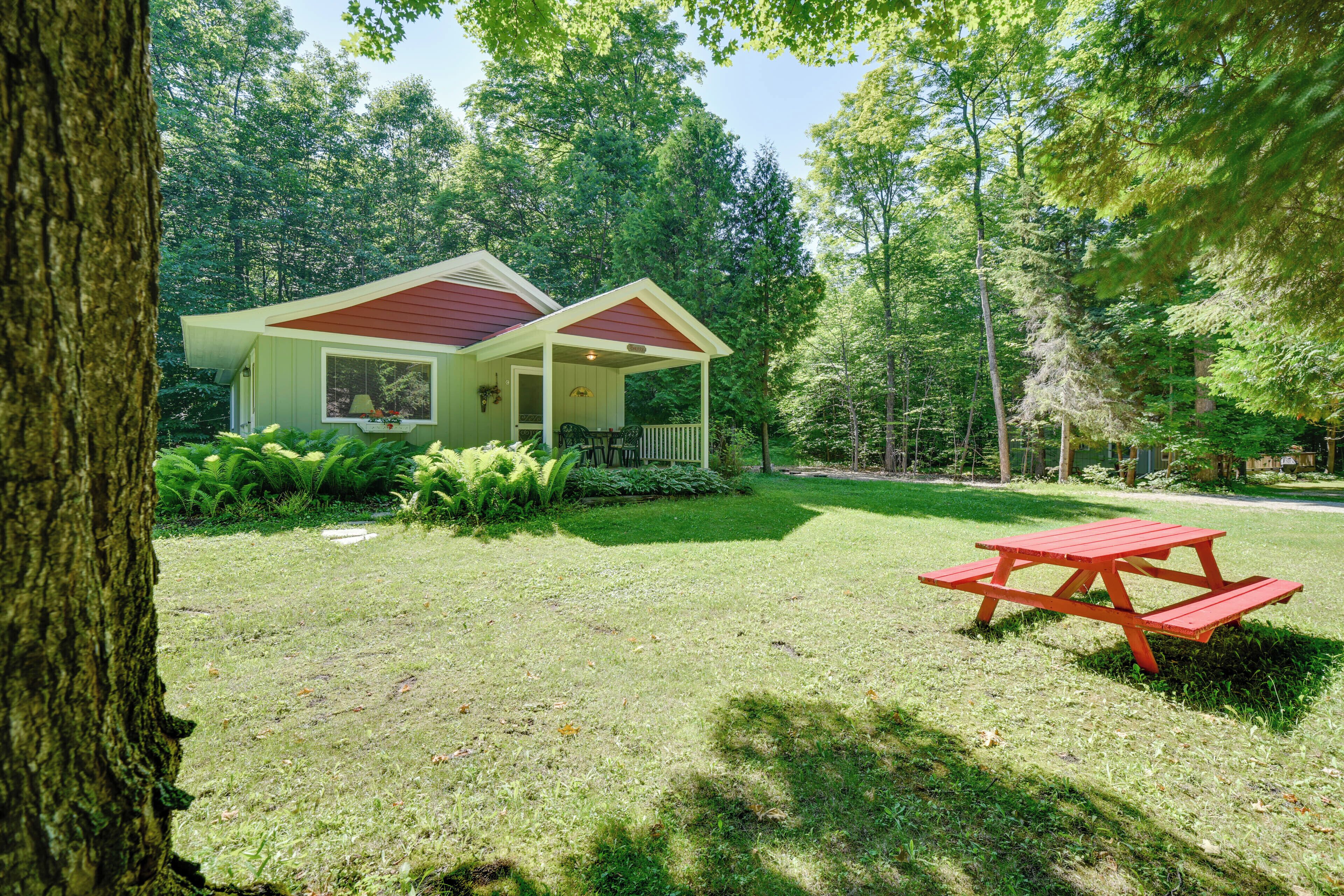 Une petite cabane avec un toit rouge, entourée d’une végétation luxuriante et une table de pique-nique au premier plan.