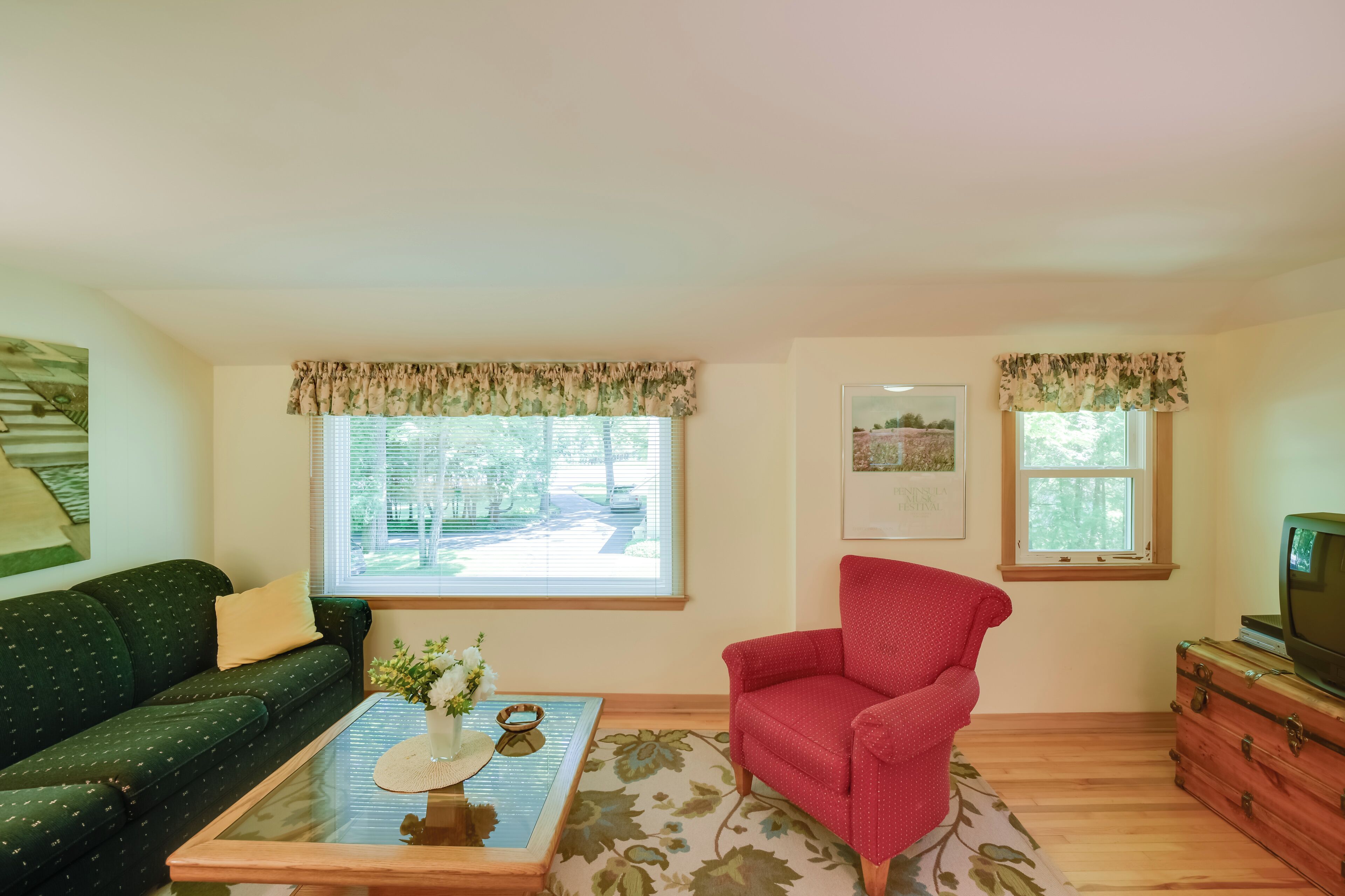 Un salón con un sofá verde, un sillón rojo, una mesa de centro con un florero y un televisor sobre un mueble de madera.