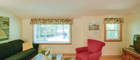 Un salón con un sofá verde, un sillón rojo, una mesa de centro con un florero y un televisor sobre un mueble de madera.