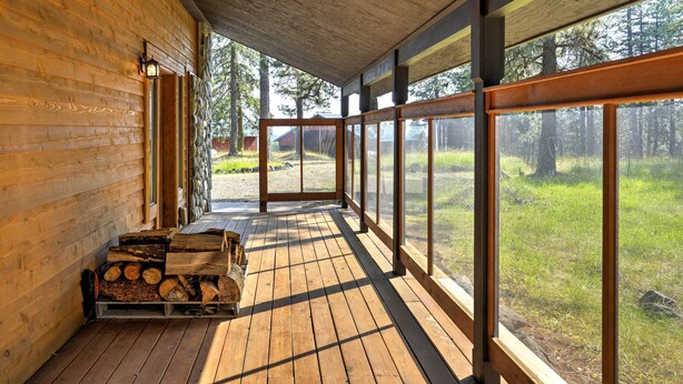 Una cabaña de madera con un porche, ventanas amplias y vistas a un bosque.