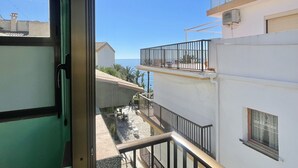 Blick aus einem Gebäude auf einen Balkon mit Geländer, ein Fenster und einen strahlend blauen Himmel.