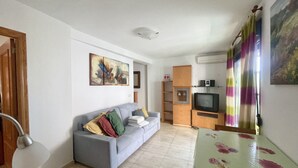 Ein Wohnzimmer mit grauem Sofa, Fernseher und einem Bild an der Wand.
