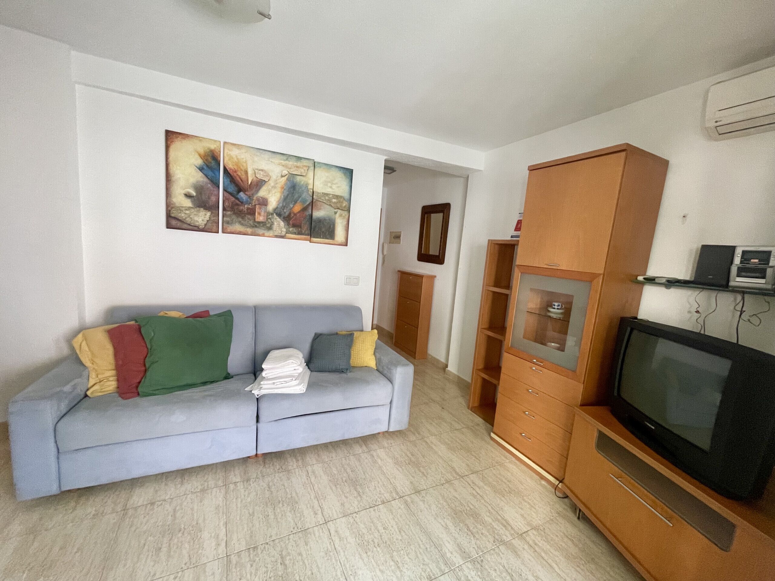 A living room with a grey sofa, a wooden cabinet, a television, and a wall-mounted painting.