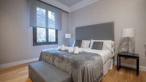 Een moderne slaapkamer met een groot bed, een nachtkastje, een vloerlamp en een raam met uitzicht op bomen.