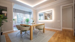 Een moderne eetruimte met een houten tafel en stoelen, een grote spiegel en uitzicht op het buitengebied door grote ramen.