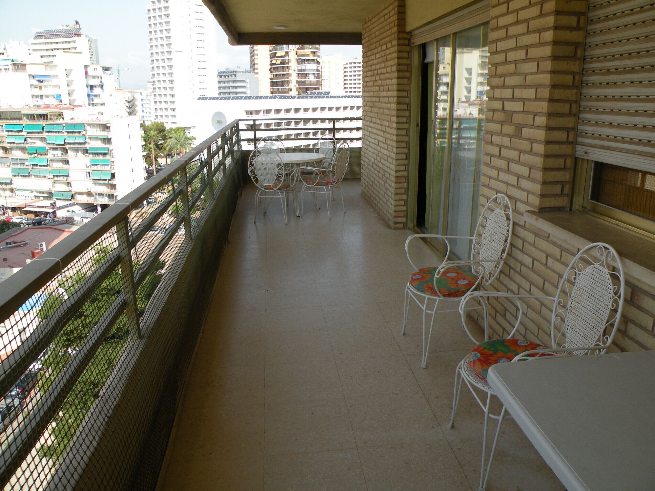 A balcony with a table and chairs, overlooking a cityscape with high-rise buildings.