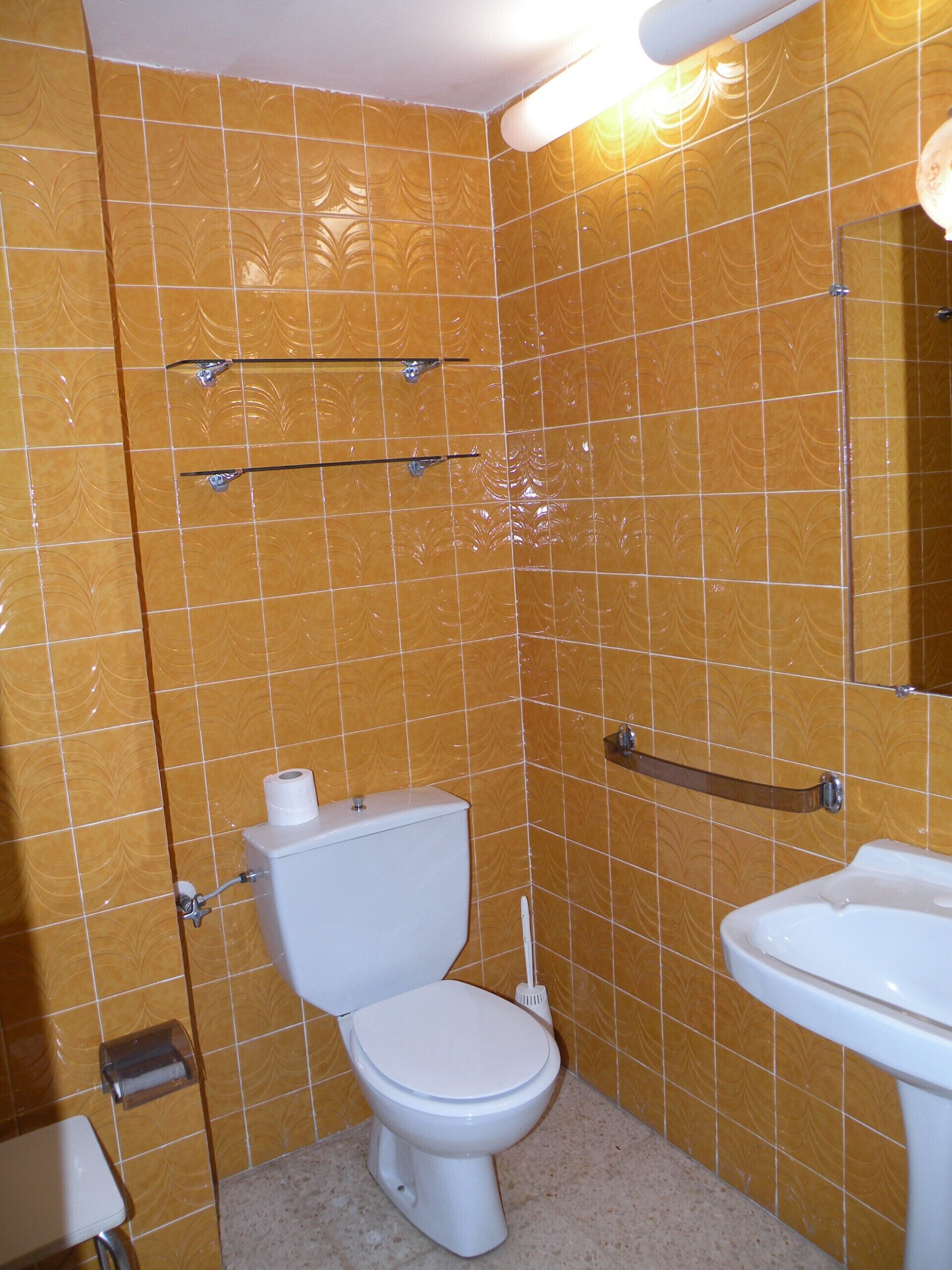 Un baño con baldosas amarillas estampadas, un inodoro blanco, un lavabo blanco y un espejo.