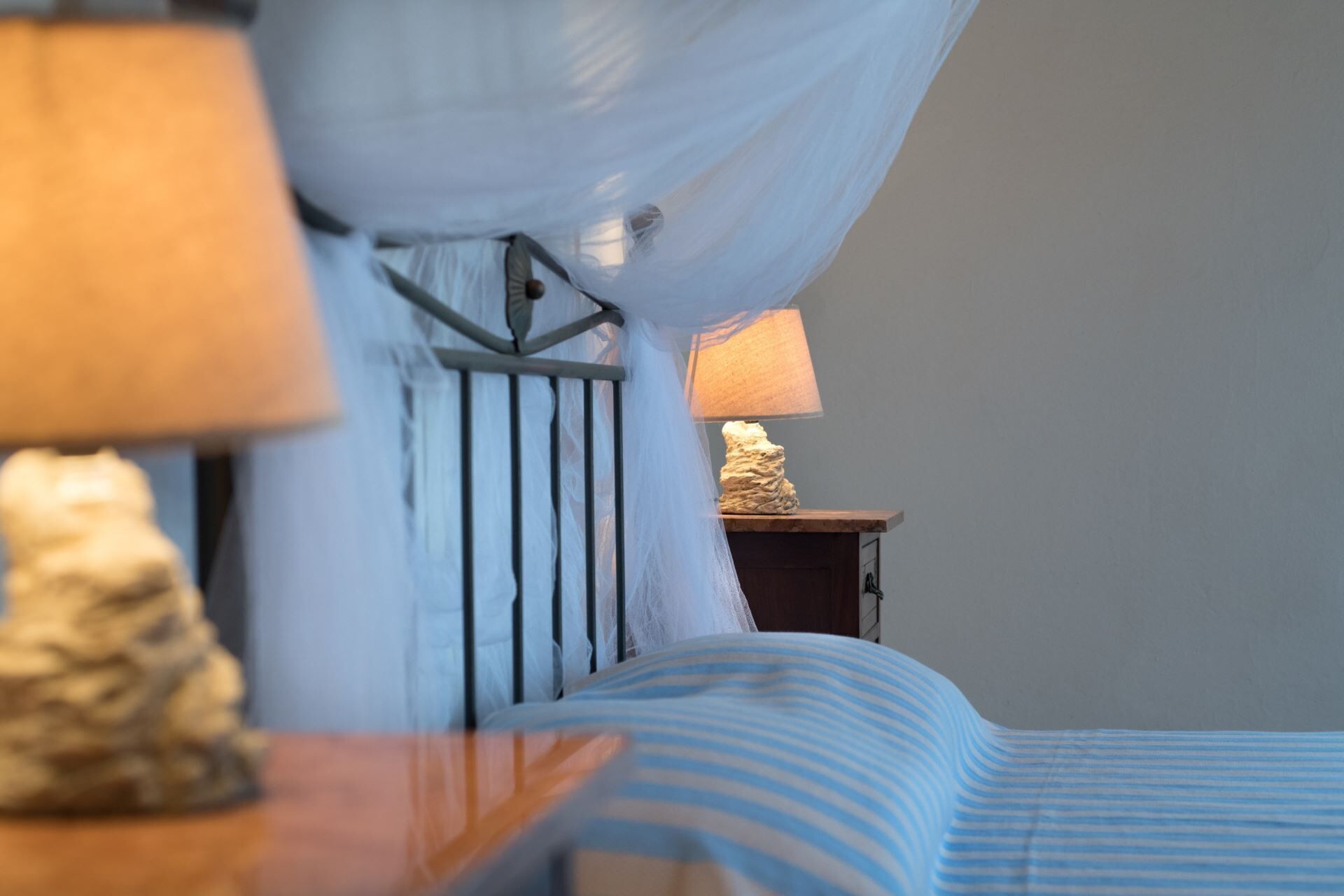 Una cama con una colcha azul a rayas, una lámpara de noche y un adorno en una mesita de madera.