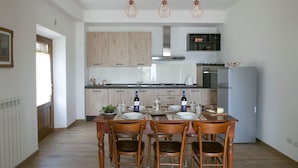 A modern kitchen with wooden cabinets, a dining table set for four, and a refrigerator. - Recently restored stone villa with private pool, ideal for couples of friends or families wishing to (Castiglion Fiorentino)