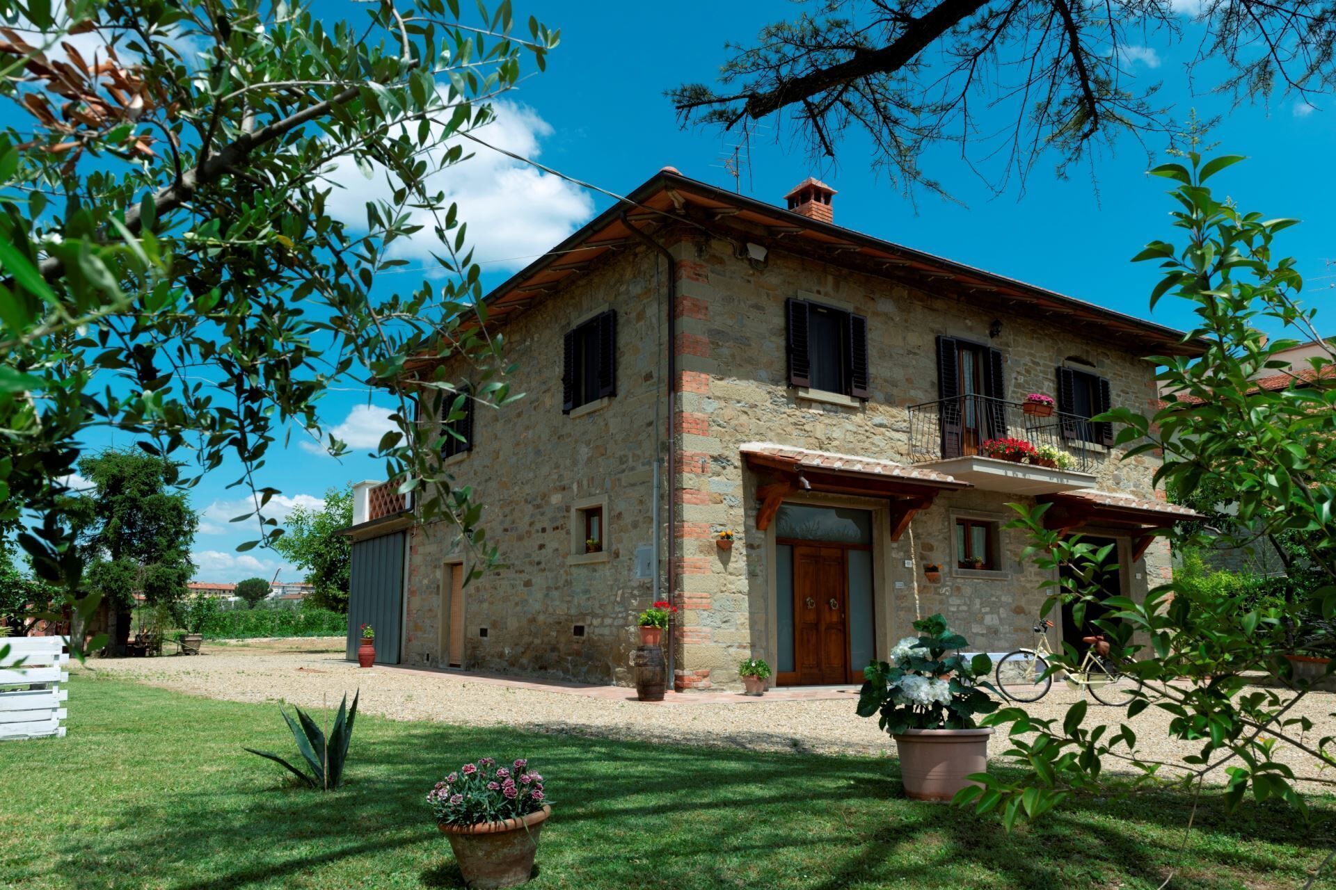 A stone house with a balcony, surrounded by greenery and a clear sky.