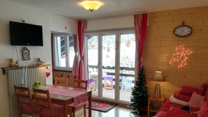 Un salon chaleureux avec un coin repas, des meubles en bois, un téléviseur et un sapin de Noël.