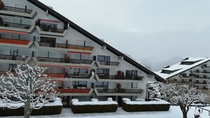 Un hôtel moderne à plusieurs étages, doté de balcons, entouré d’arbres couverts de neige et offrant une vue sur un paysage montagneux.