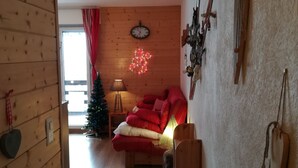 Une pièce chaleureuse aux murs en bois, un lit avec une literie rouge, un petit sapin de Noël et une horloge fixée au mur.