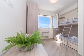 A compact room with bunk beds, a potted plant, a window with a view, and a built-in air conditioning unit. - Serena 2 Amazing Sea View, Alassio, Italy (Alassio)