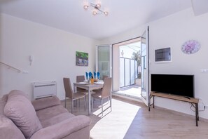 A modern living room with a sofa, dining table, chairs, a TV, and a sliding glass door leading to an outdoor area. - Serena 2 Amazing Sea View, Alassio, Italy (Alassio)