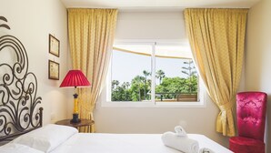 Ein Hotelzimmer mit einem Bett, zwei aufgerollten Handtüchern, einer roten Lampe, einem roten Sessel und einem Fenster mit gelben Vorhängen.