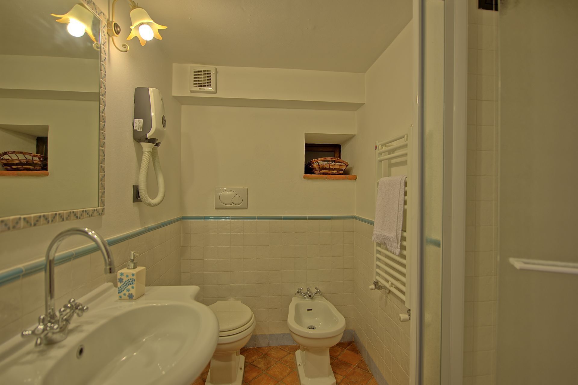 A bathroom with a sink, toilet, bidet, and a mirror with a light fixture.