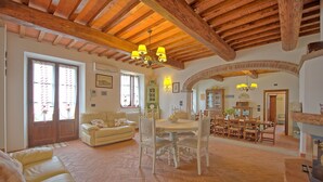 A spacious living room with a high wooden ceiling, a dining area with wooden furniture, and a fireplace. - Villa Farneta - Villa with private pool (Cignano)