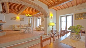 A spacious living area with a high ceiling, exposed wooden beams, a fireplace, and a dining table with chairs. - Villa Farneta - Villa with private pool (Cignano)