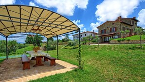 A covered outdoor seating area with a table and benches, a stone patio, and a stone house in the background. - Villa Farneta - Villa with private pool (Cignano)
