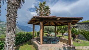 A wooden gazebo with a stone base, surrounded by lush greenery and palm trees, overlooking a mountainous landscape. - Villa La Pace, Charming 3 bedroom villa with private pool with views of Amalfi Coast (Sant'Agnello)
