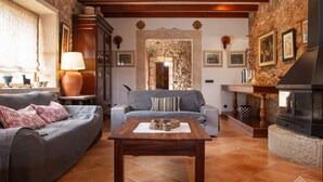 Una sala de estar acogedora con pared de piedra, vigas de madera, chimenea y suelo de baldosas.