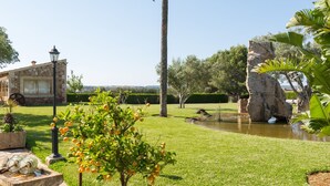 Un jardín bien cuidado con una palmera, un pequeño estanque y un edificio de piedra con una ventana.
