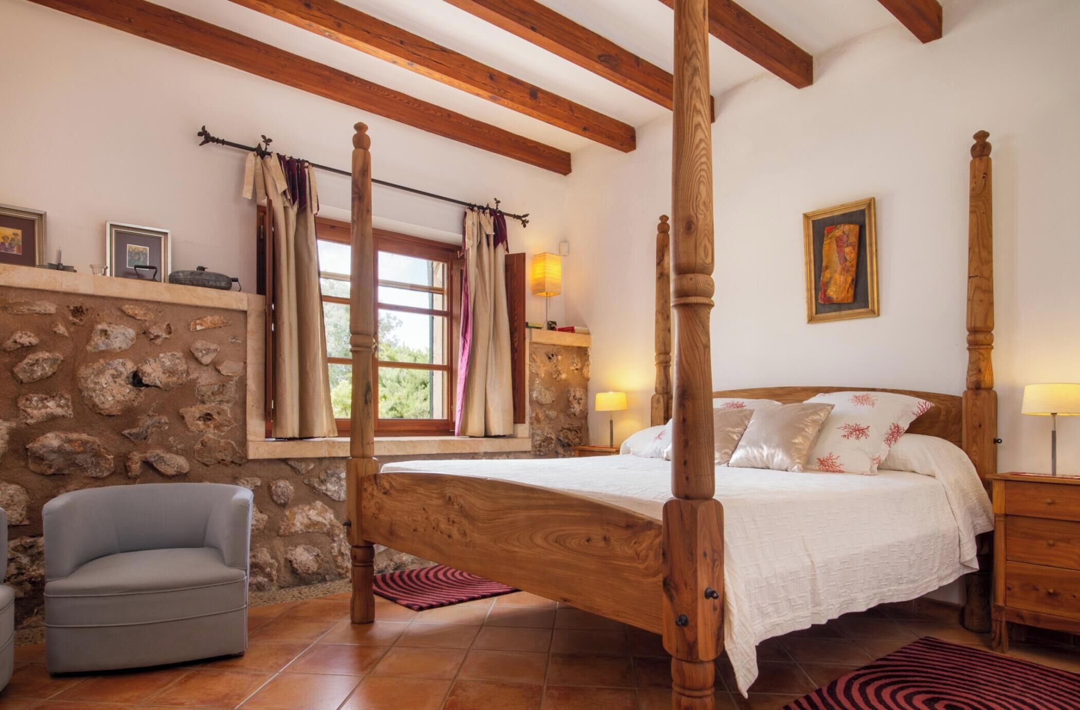 Une chambre à coucher avec un lit à baldaquin, un mur en pierre, des poutres apparentes et une fenêtre avec des rideaux.
