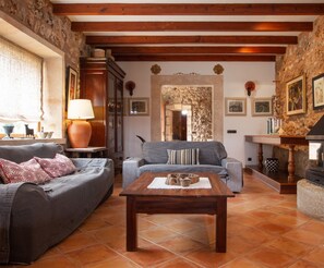 Ein gemütliches Wohnzimmer mit Steinwand, Holzbalken, Kamin und Fliesenboden.