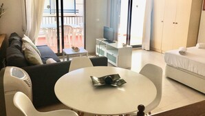 A hotel room with a sofa, a small table with a remote control, a bed with a neatly made white bedspread, and a balcony with a table and chairs. - SAN ROC APARTMENT R035 (Benidorm)
