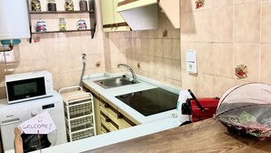 A compact kitchen with a sink, microwave, and a washing machine. There are shelves with jars and a small decorative item on the wall. - SAN ROC APARTMENT R035 (Benidorm)