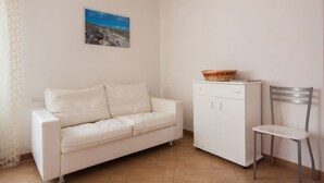 A white sofa, a white cabinet, and a metal chair in a room with a tiled floor.