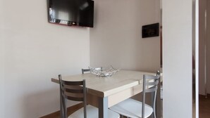 A dining area with a wooden table, two chairs, a metal tray, a flat-screen TV mounted on the wall, and a small framed picture on the wall.