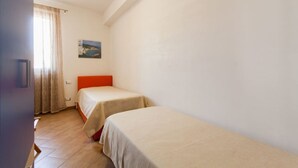 A room with two single beds, a painting on the wall, and a window with curtains.