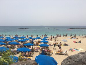 Una playa con numerosos sombrillas azules y tumbonas.
