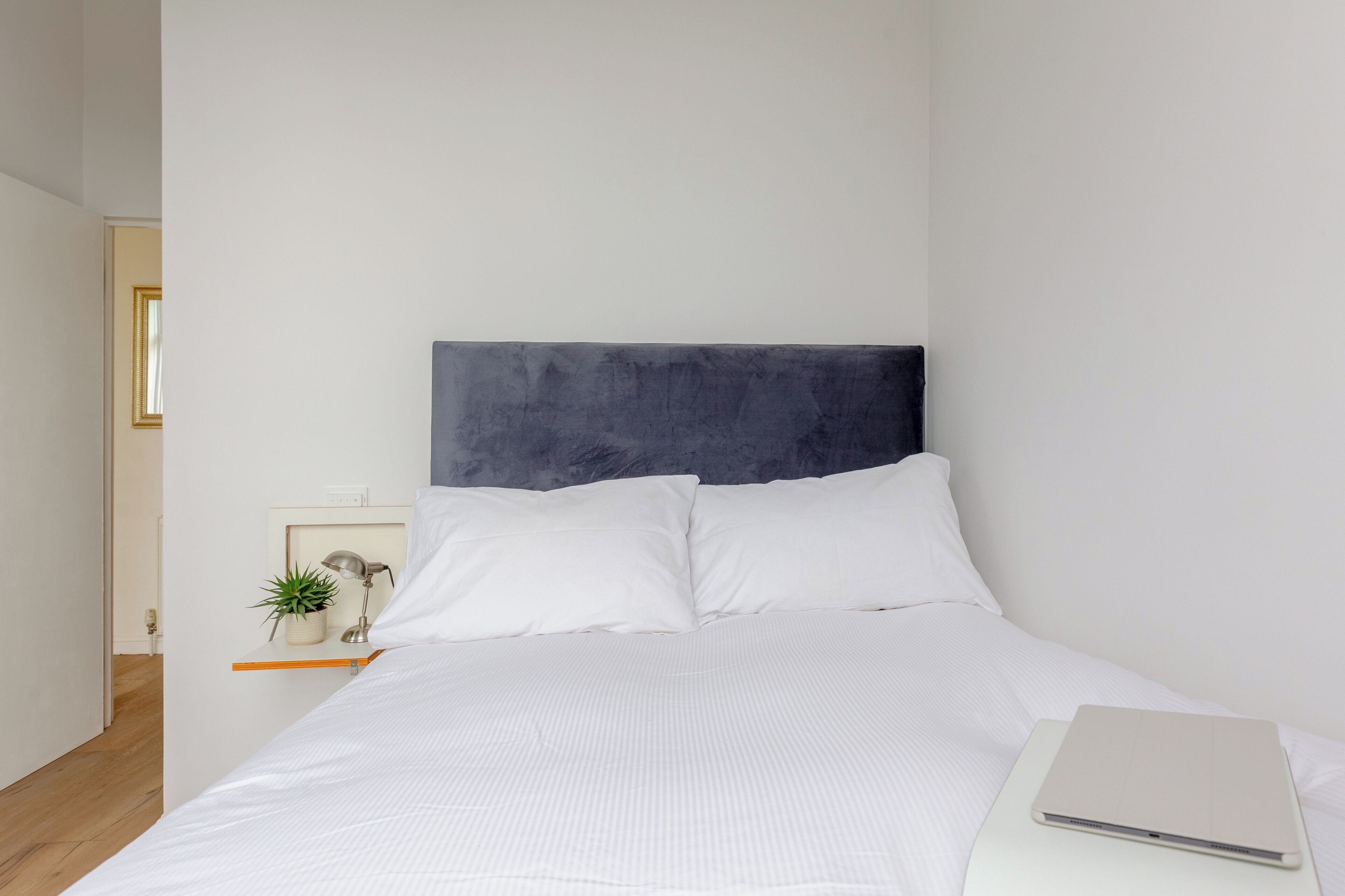 Una cama bien hecha con ropa de cama blanca y un ordenador portátil a un lado.